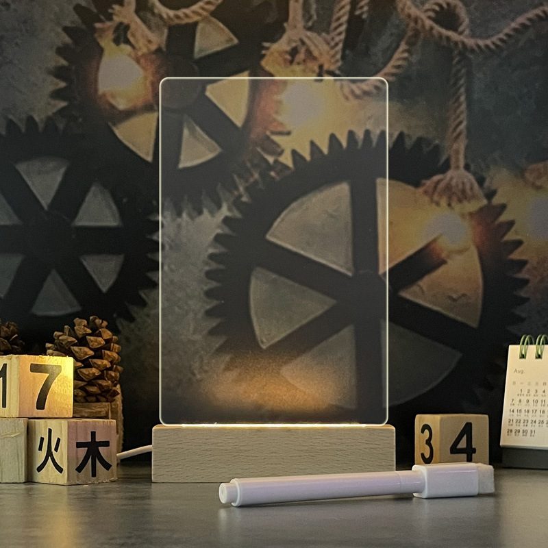 A clear Glowboard on a wooden base with a pen, lit warmly on a desk